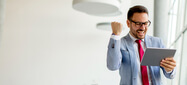 Hombre con gafas, tiene una tableta en la mano, al mirar la tableta genera gesto de celebración